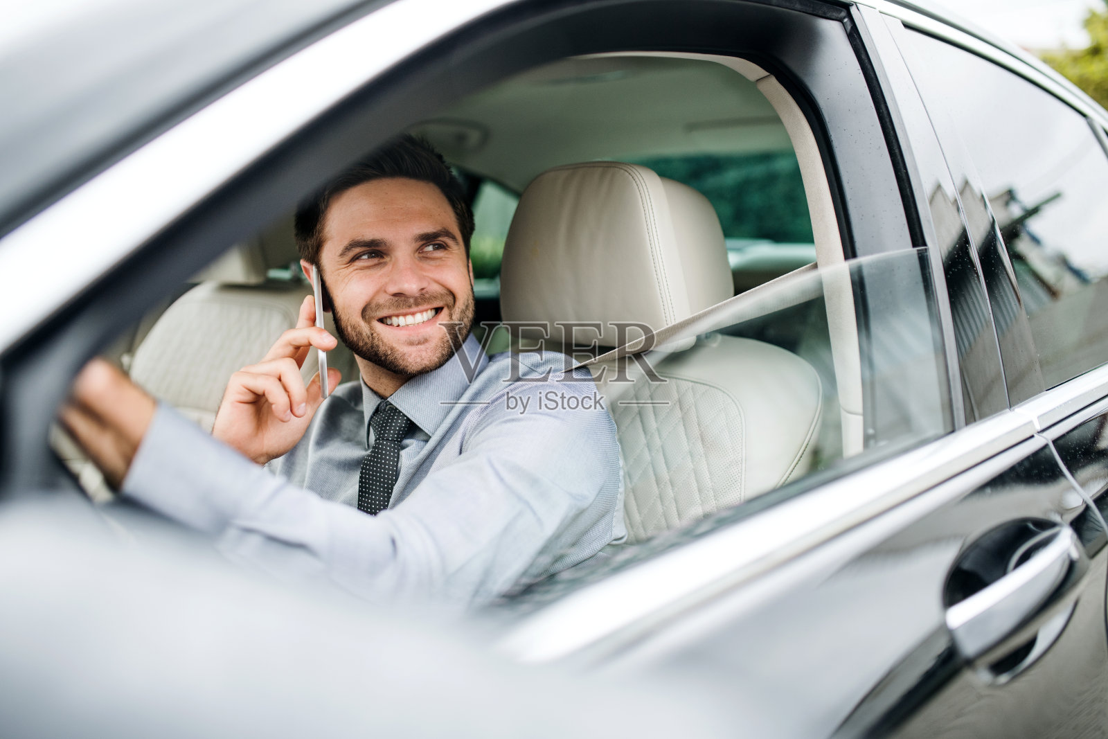 年轻的商人，穿着衬衫，打着领带，拿着手机坐在车里。照片摄影图片