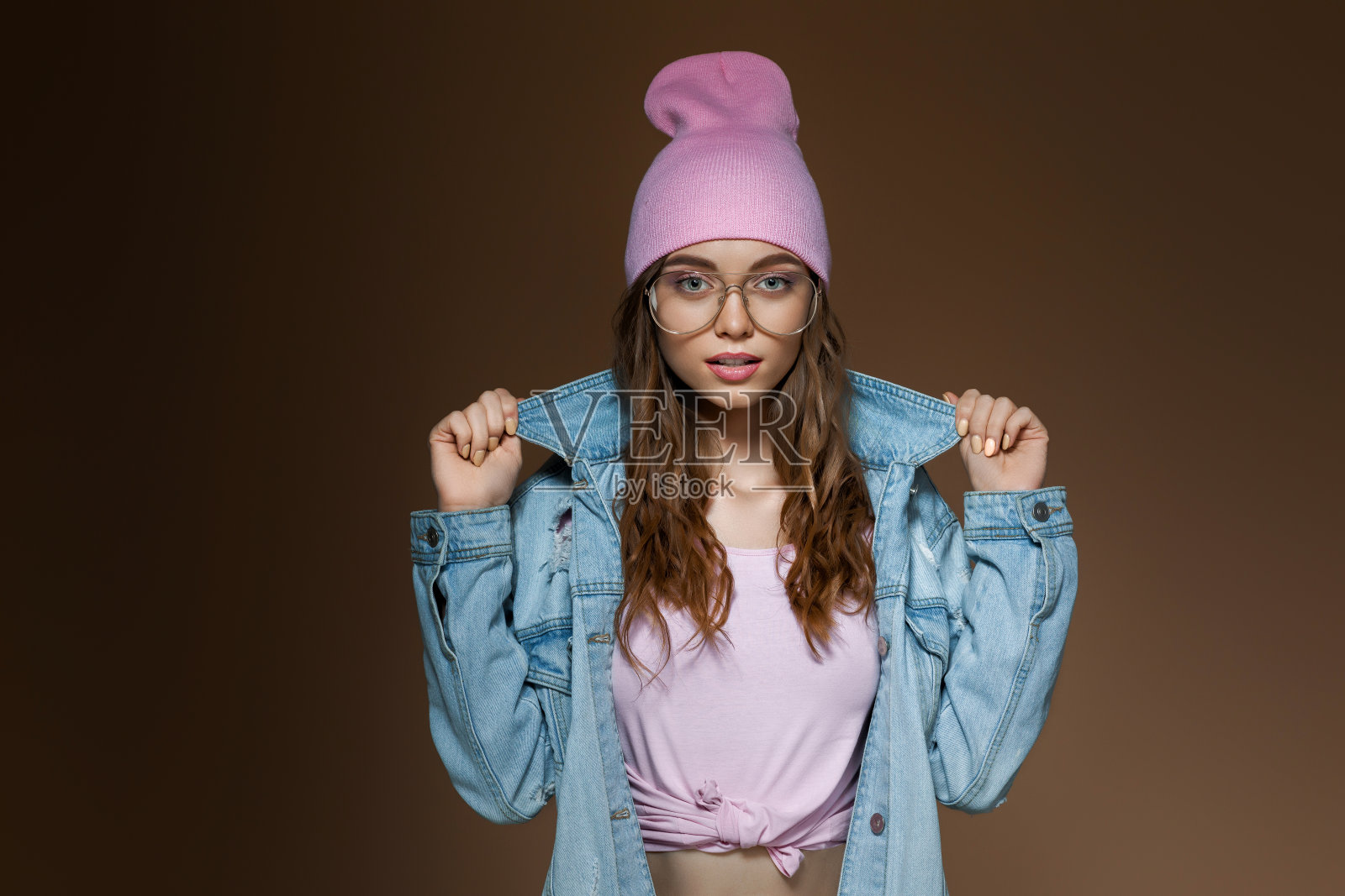 女孩穿着牛仔裤夹克，粉红色的帽子和时尚的眼镜照片摄影图片