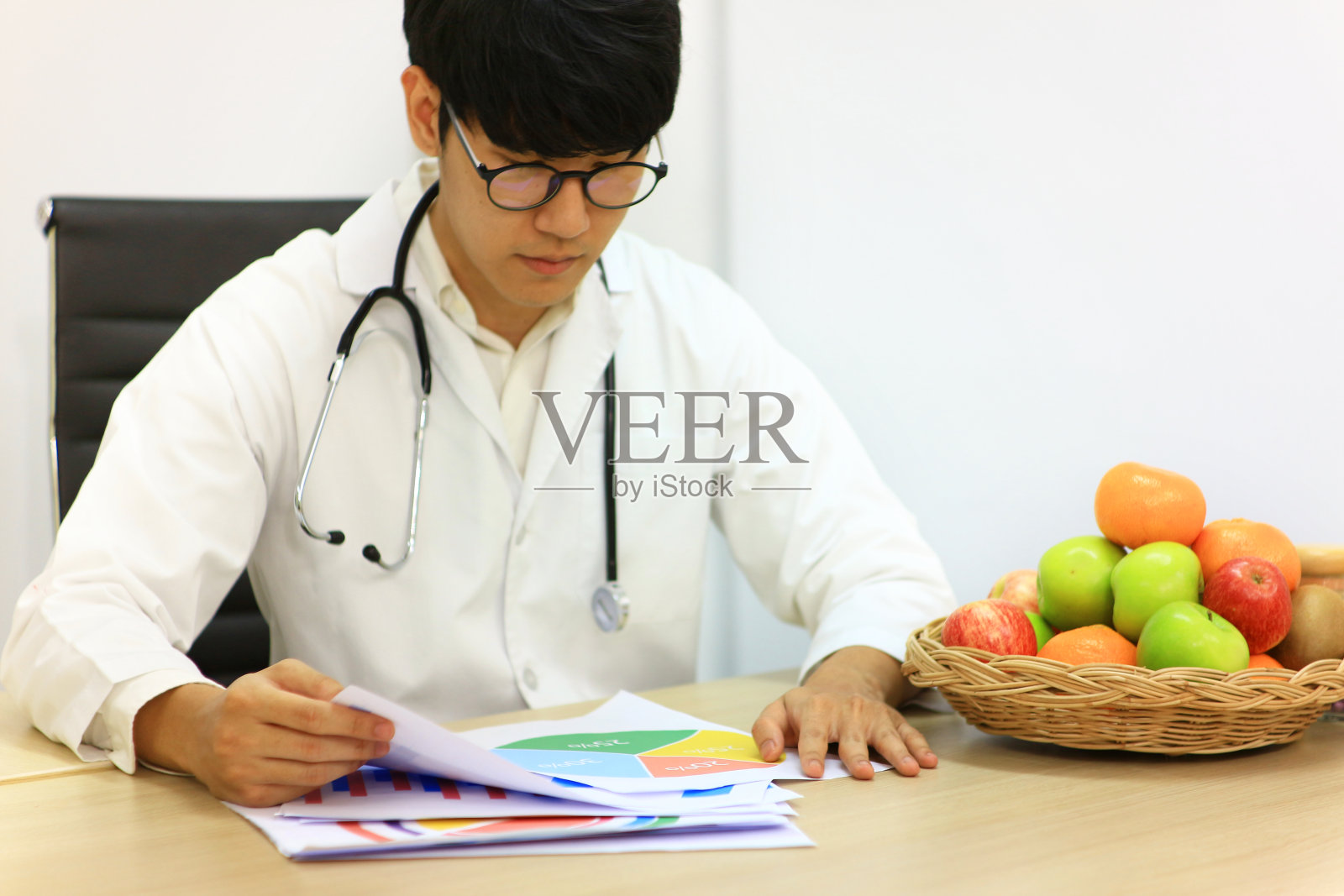 亚洲医生在桌子上工作，桌子上有数据纸和水果在篮子里。照片摄影图片