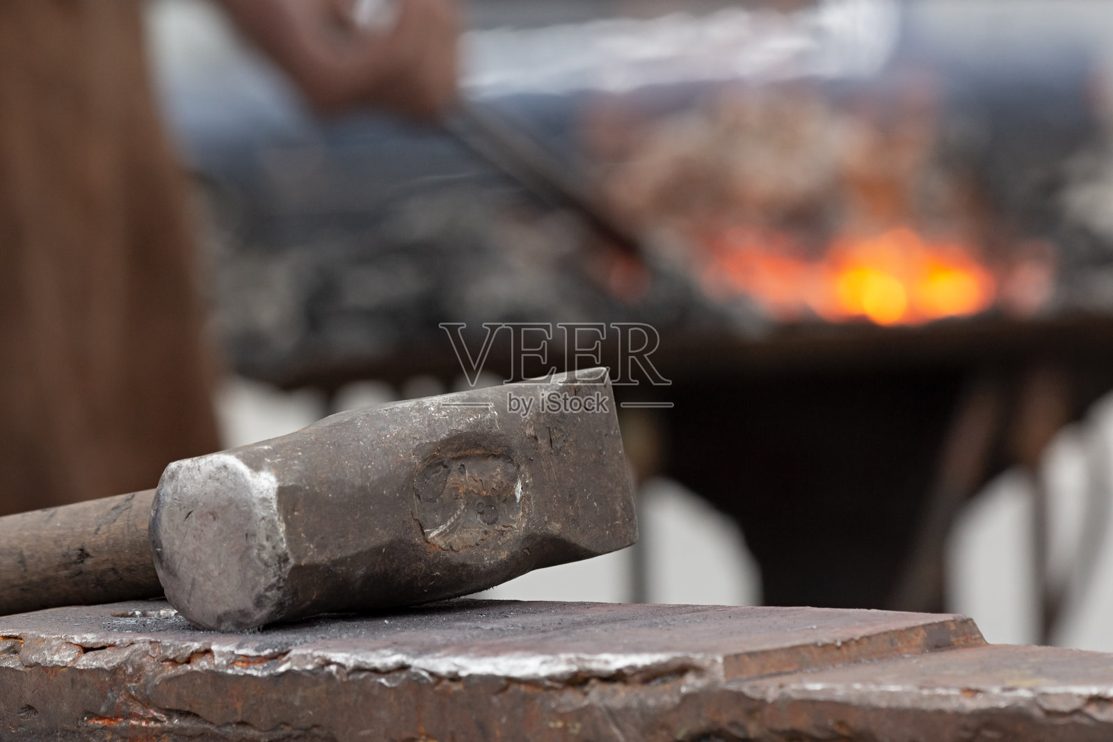 生锈的旧锤子躺在铁砧上，背景是铁炉上的铁匠工作。照片摄影图片