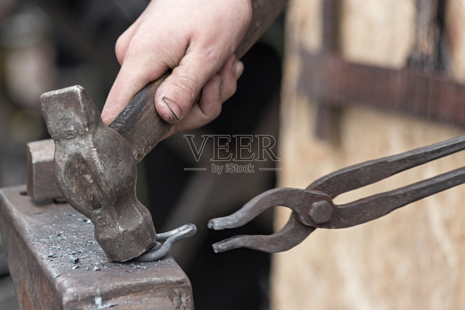 铁匠用锤子和钳子打一个铁圈。照片摄影图片