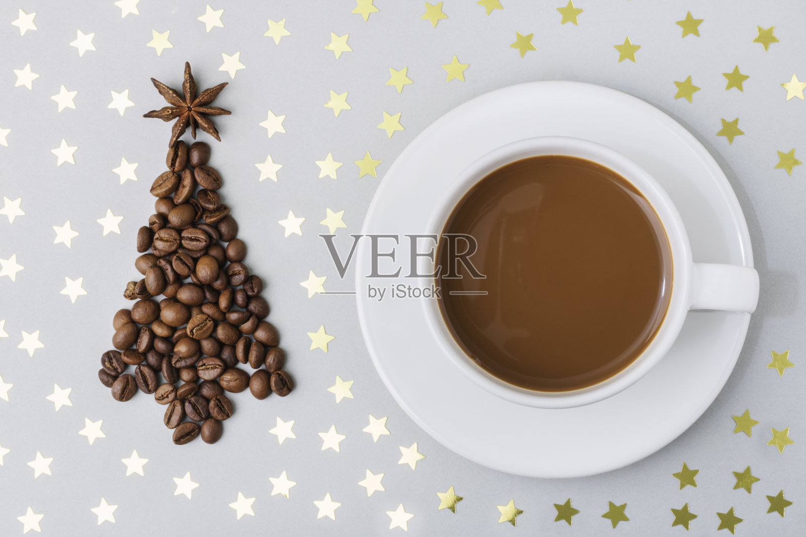 桌上放着一杯热咖啡，灰色的背景上点缀着金色的星星，旁边是一棵用咖啡豆做成的圣诞树。圣诞节和新年的概念。前视图。本空间照片摄影图片