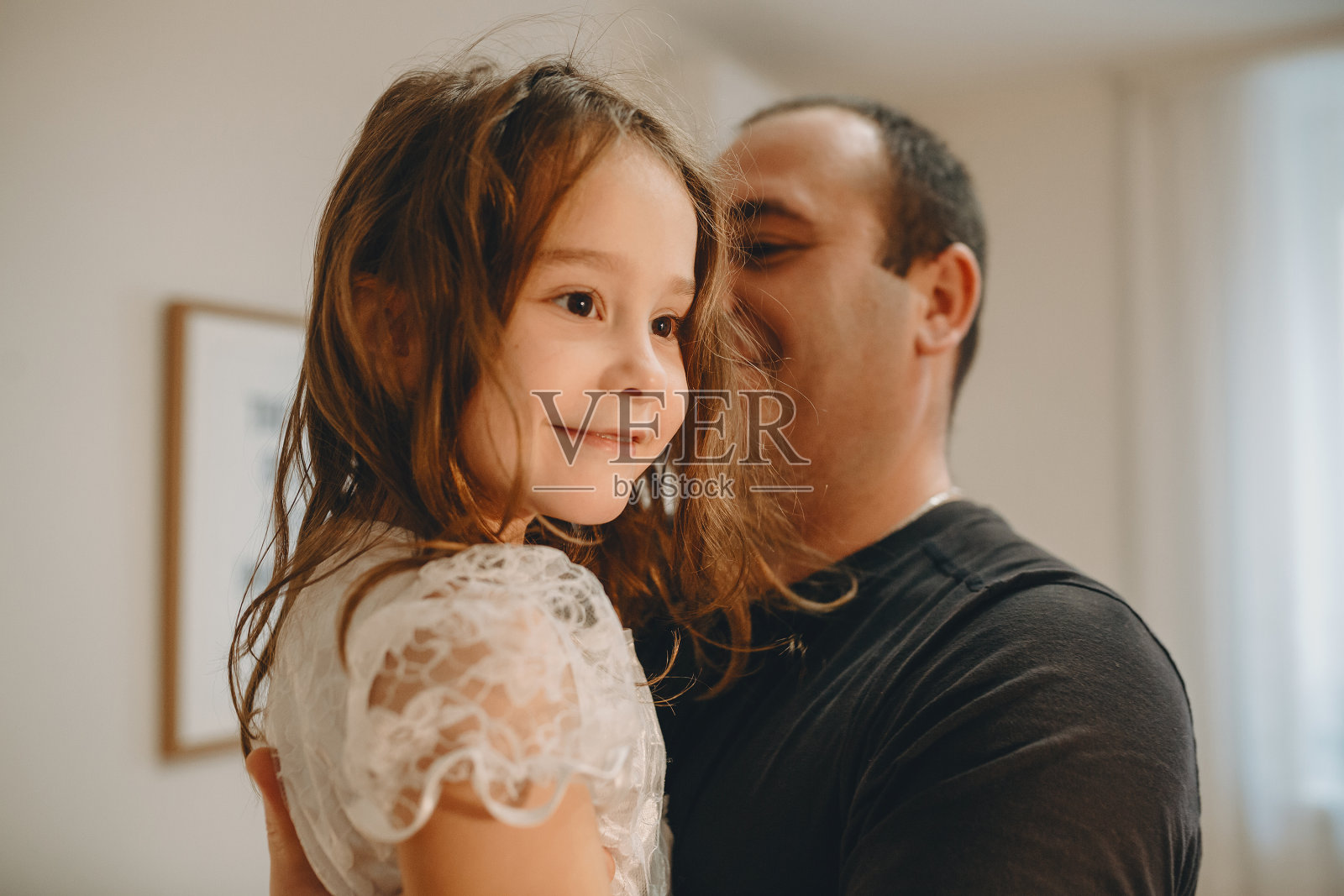近距离的肖像可爱的女孩看着远离微笑，而她的父亲在家里。照片摄影图片