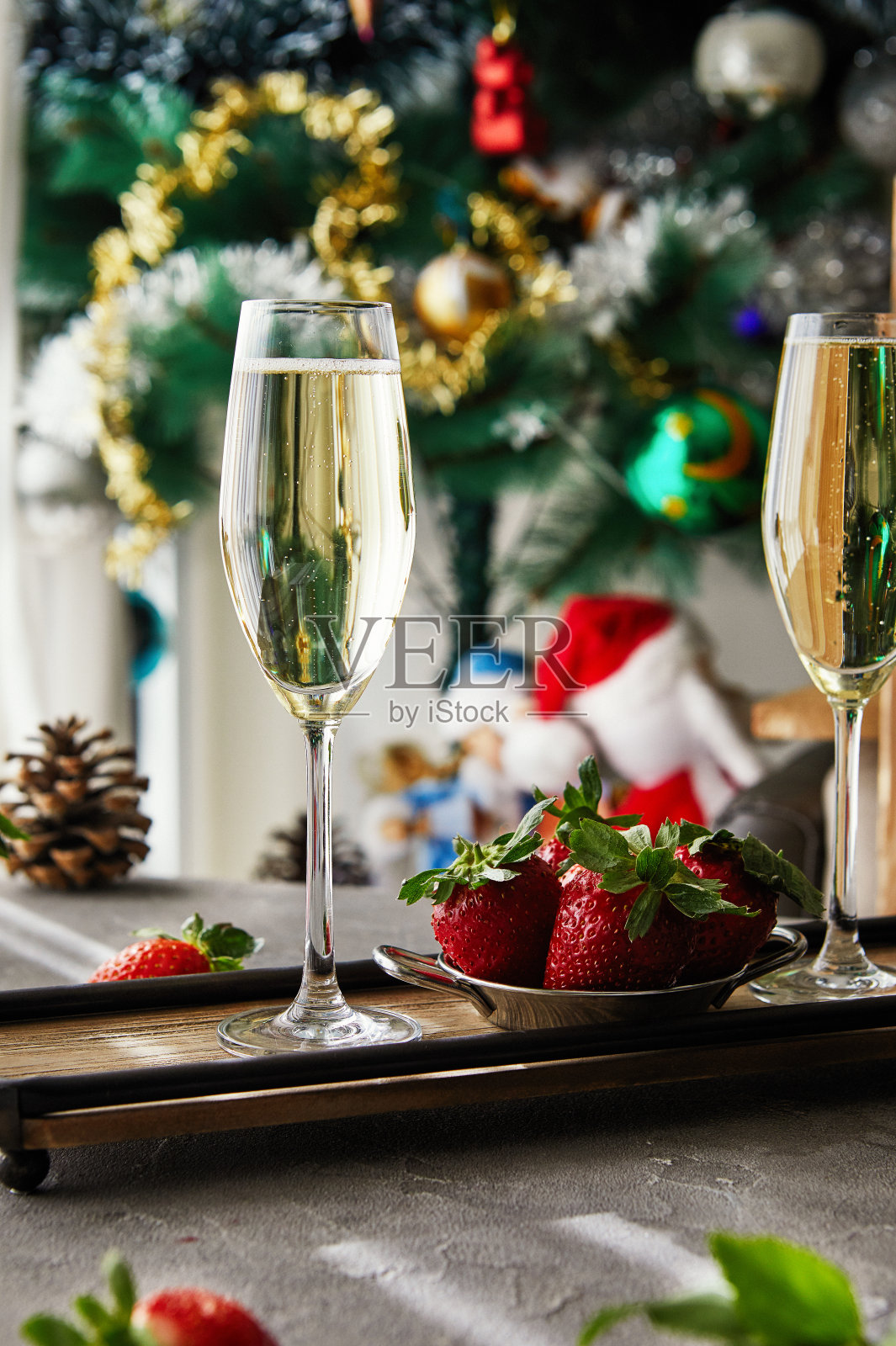 灰色背景上放着香槟和草莓的玻璃杯，背景是一棵圣诞树照片摄影图片