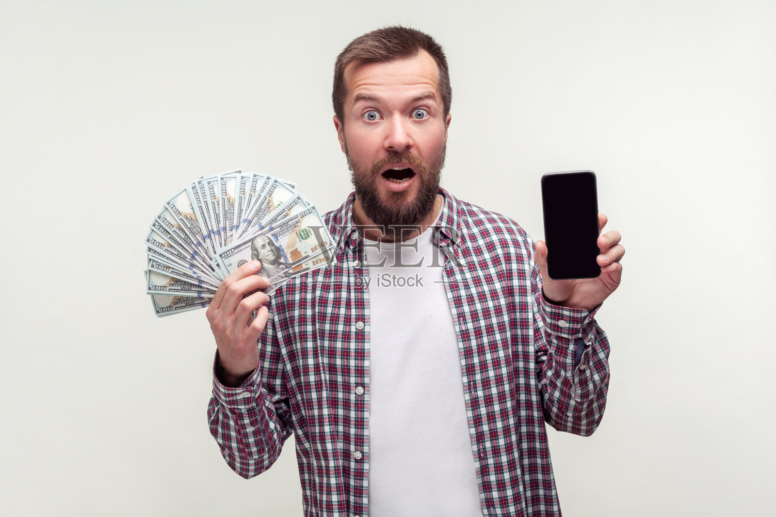 手机银行应用。一名胡须胡须的男子手持智能手机和一大笔钱。白色背景照片摄影图片