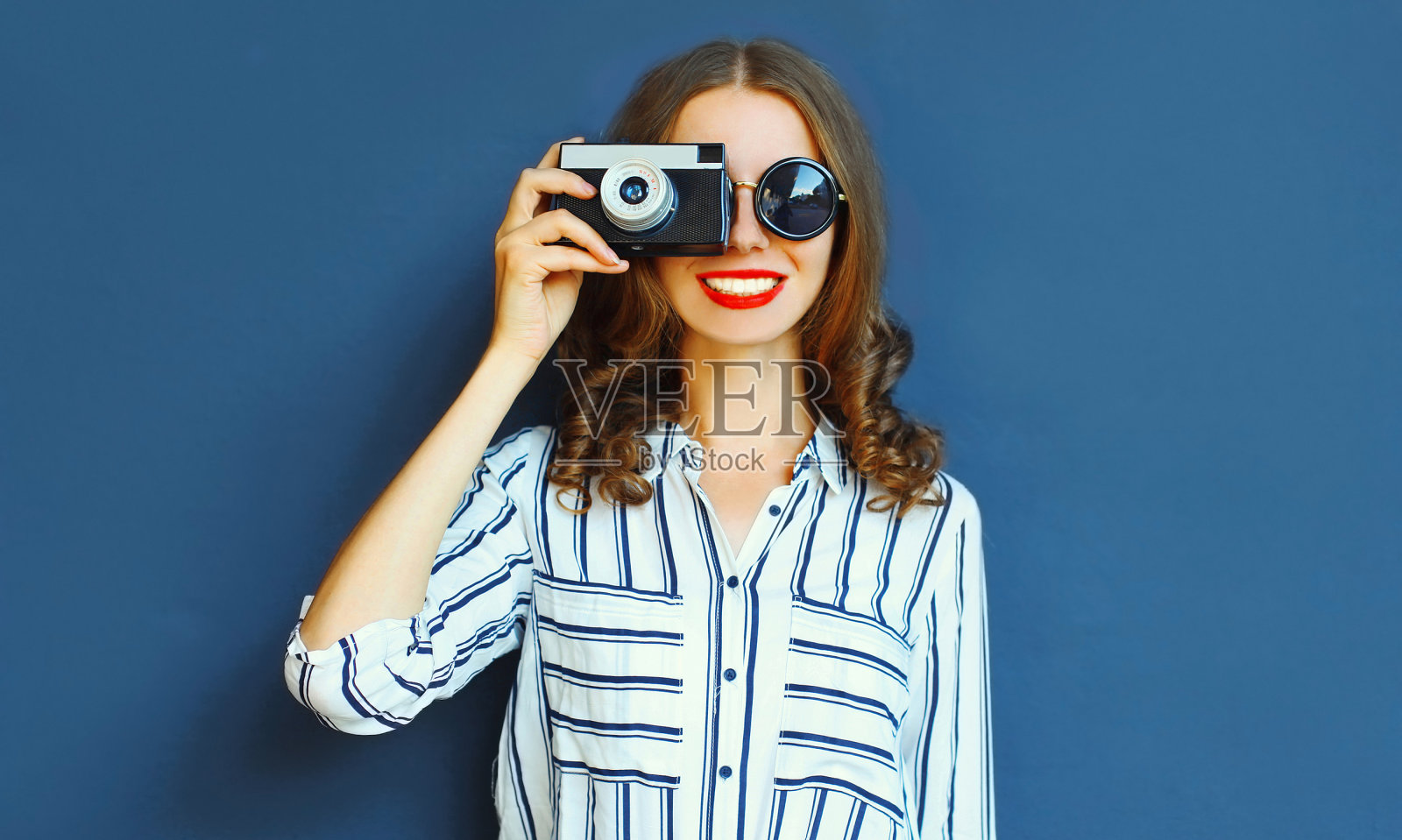 肖像微笑的年轻女性摄影师与老式电影相机在蓝色的墙壁背景照片摄影图片