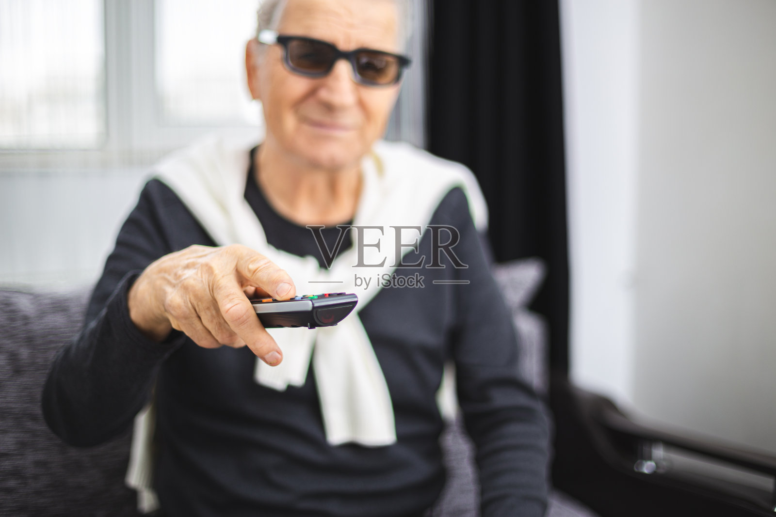 戴着3D眼镜，拿着电视遥控器的老人照片摄影图片