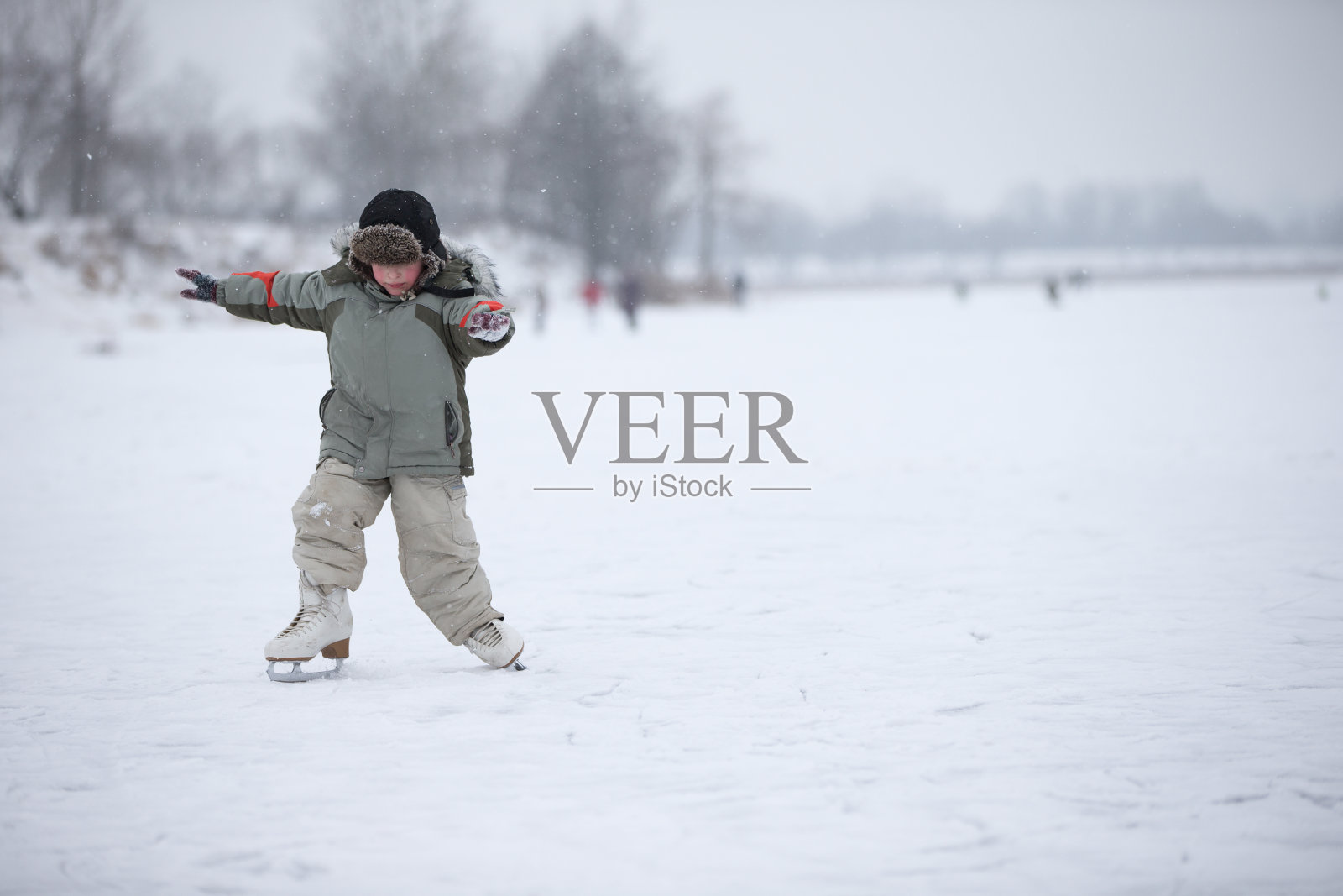 这孩子学在湖上溜冰。在一个下雪的冬日，一个男孩在冰河上滑冰照片摄影图片