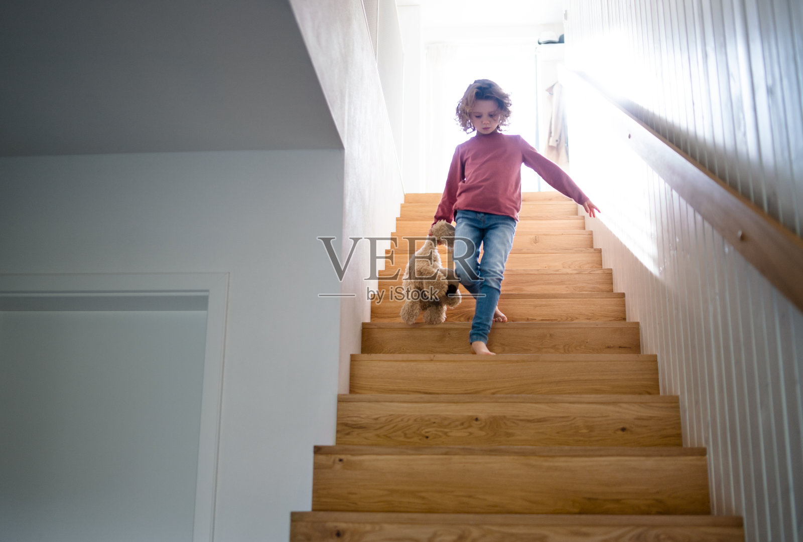 一个可爱的小女孩走下家里的木楼梯。照片摄影图片