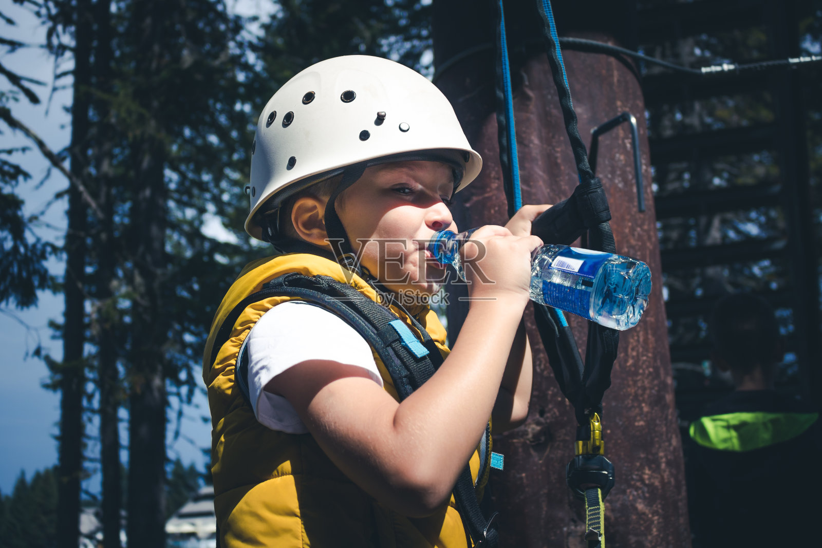 口渴的男孩在冒险公园的树梢上休息时喝水。照片摄影图片