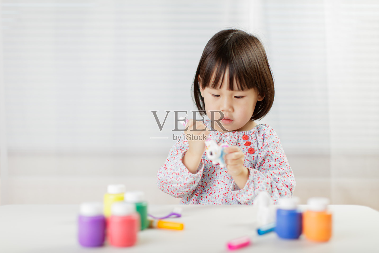 蹒跚学步的小女孩在家里的动物玩具上画水彩画，以白色为背景照片摄影图片