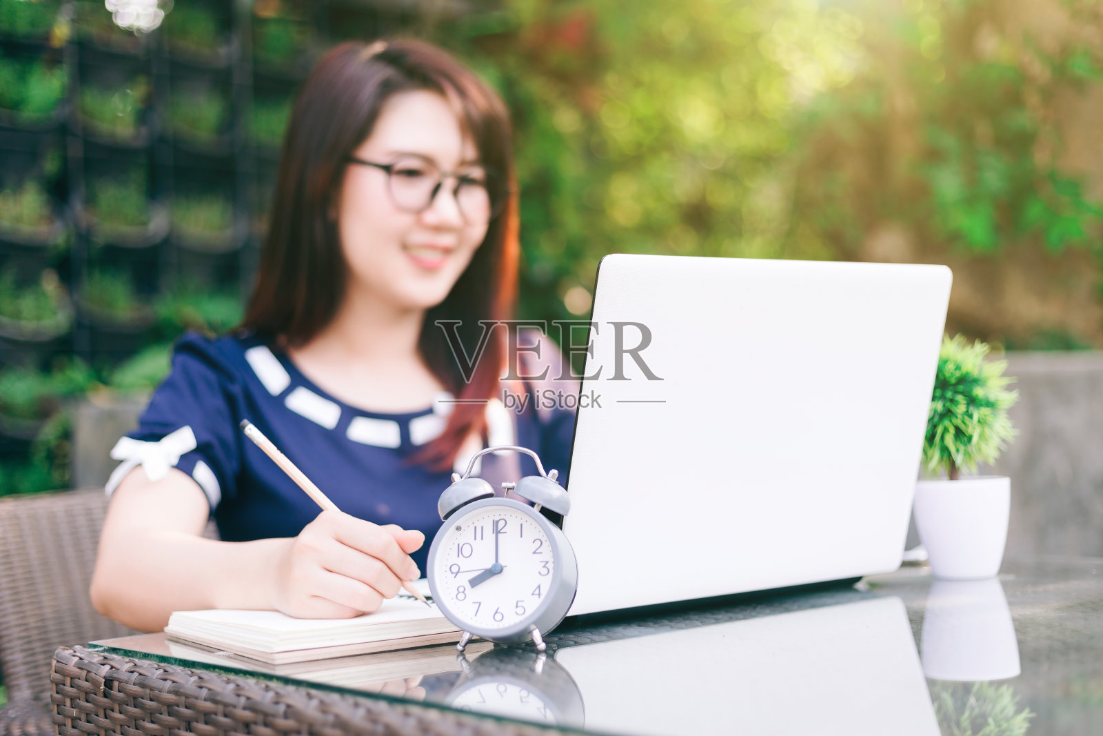 特写时钟与商务女性工作与笔记本电脑做笔记在夏季公园的背景。照片摄影图片