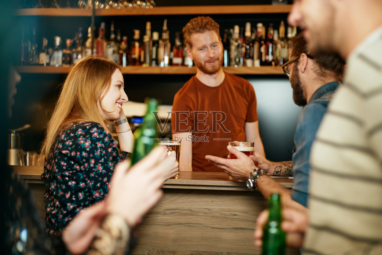 一群最好的朋友站在酒吧里，喝啤酒，聊天，玩乐。专注于调酒师擦拭酒杯。夜生活。照片摄影图片