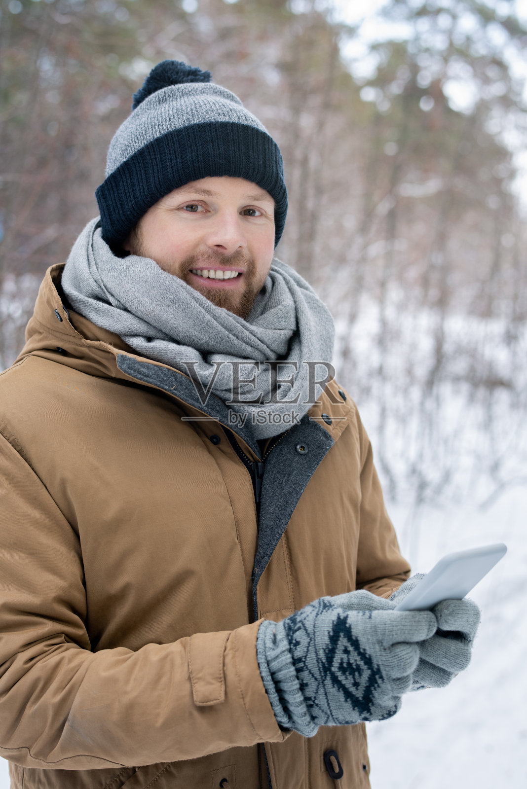年轻人戴着灰色的无檐帽，围巾，手套保暖夹克在智能手机上滚动照片摄影图片