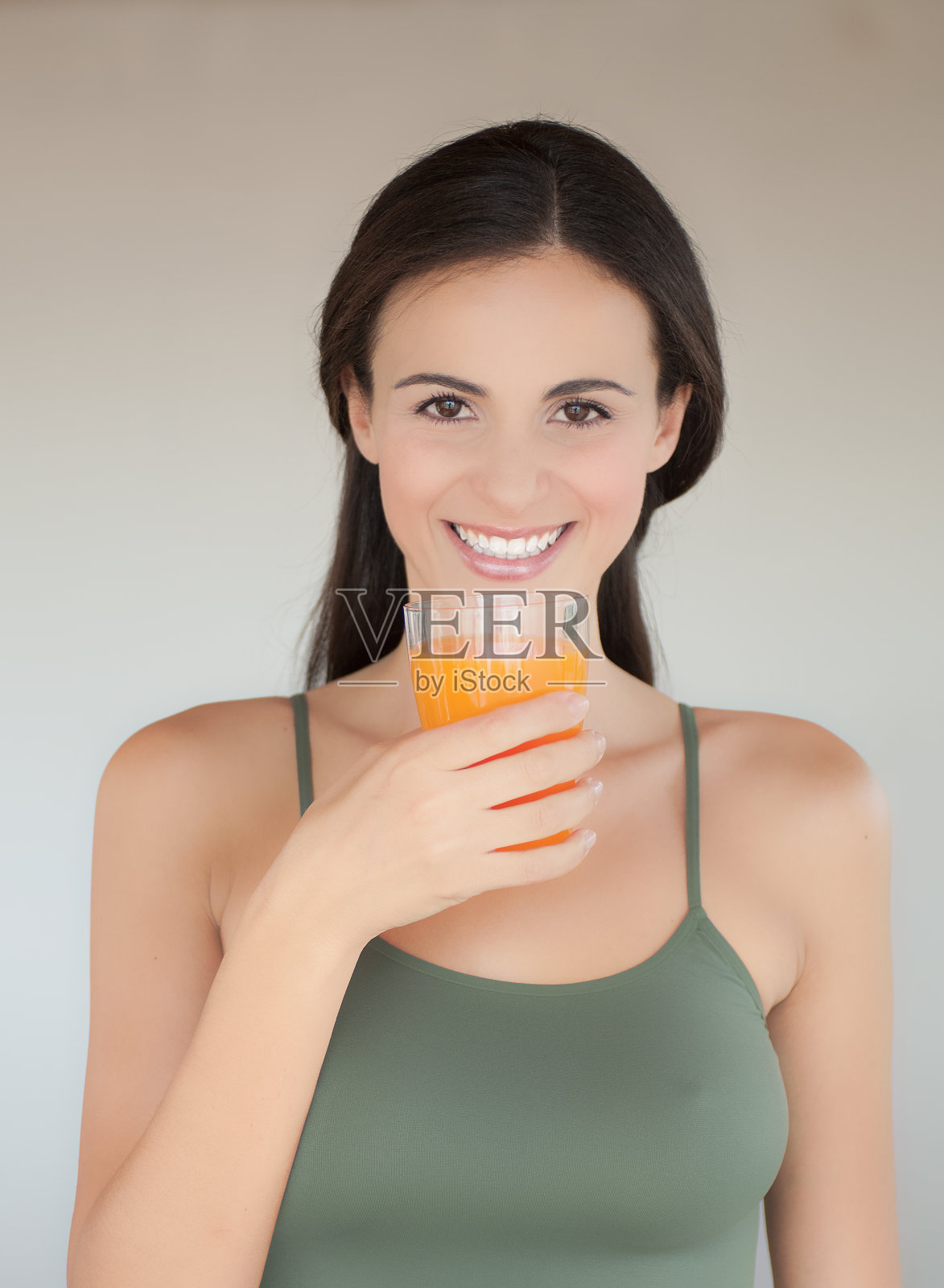 年轻的女人微笑着，一只手拿着一杯橙汁照片摄影图片