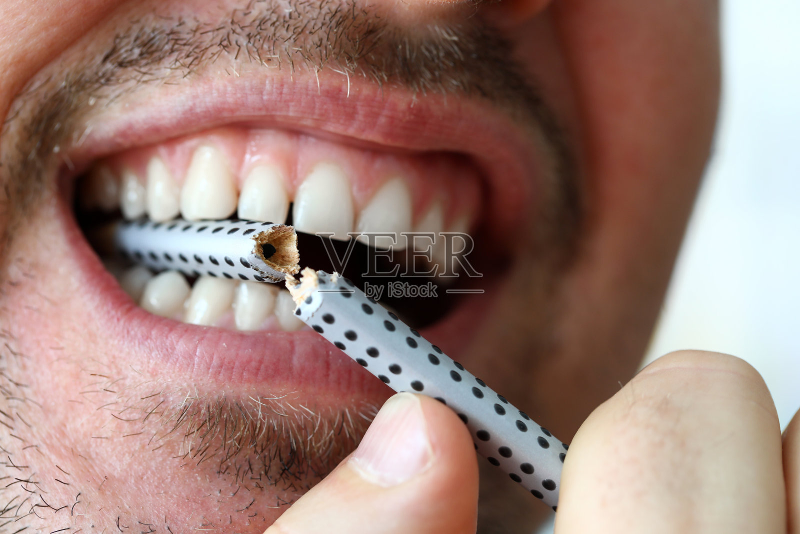 一个愤怒的人用嘴叼着灰色的铅笔，用牙齿把它咬断照片摄影图片