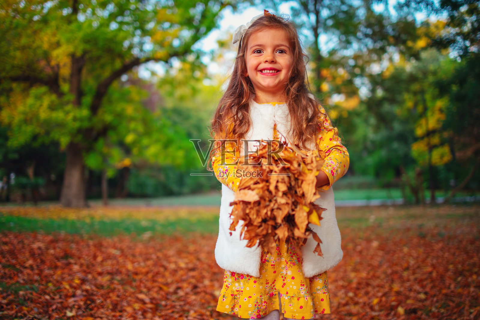 微笑的小女孩在阳光公园里玩秋天的树叶照片摄影图片