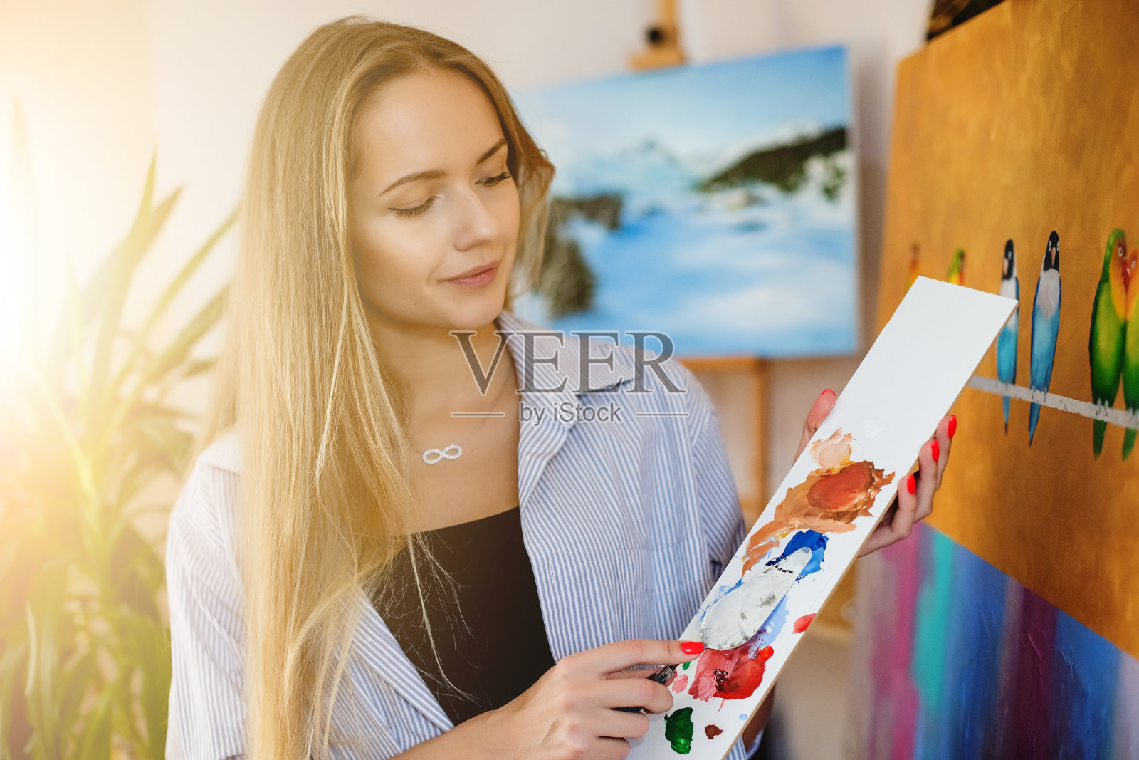美丽的白人妇女在室内画图画。用画笔和颜料工作。平板电脑和画架。温暖的室内氛围。周围柔和的光线照片摄影图片