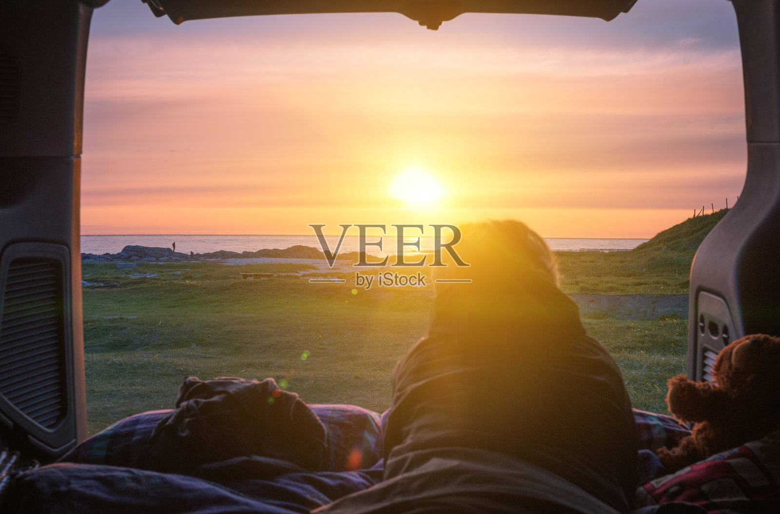 一个人坐在汽车后备箱里看着海面上的夕阳照片摄影图片