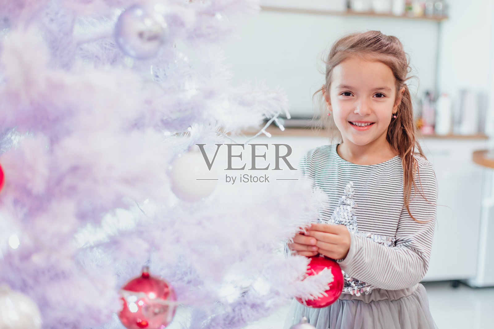 一个黑发的小女孩正在家里用五颜六色的小饰物装饰一棵人造圣诞树。照片摄影图片
