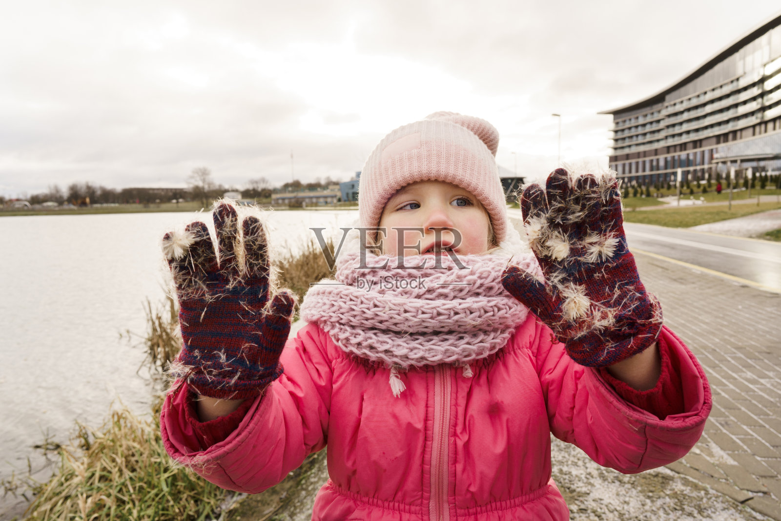 一个4岁的小女孩戴着冬天的帽子和夹克，双手戴着带有芦苇绒毛的手套照片摄影图片