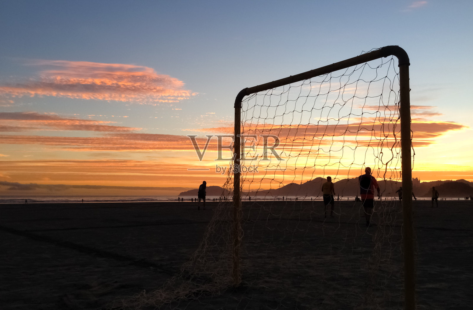 一群朋友在沙滩上踢足球在一个壮丽的夏天日落在桑托斯，巴西照片摄影图片