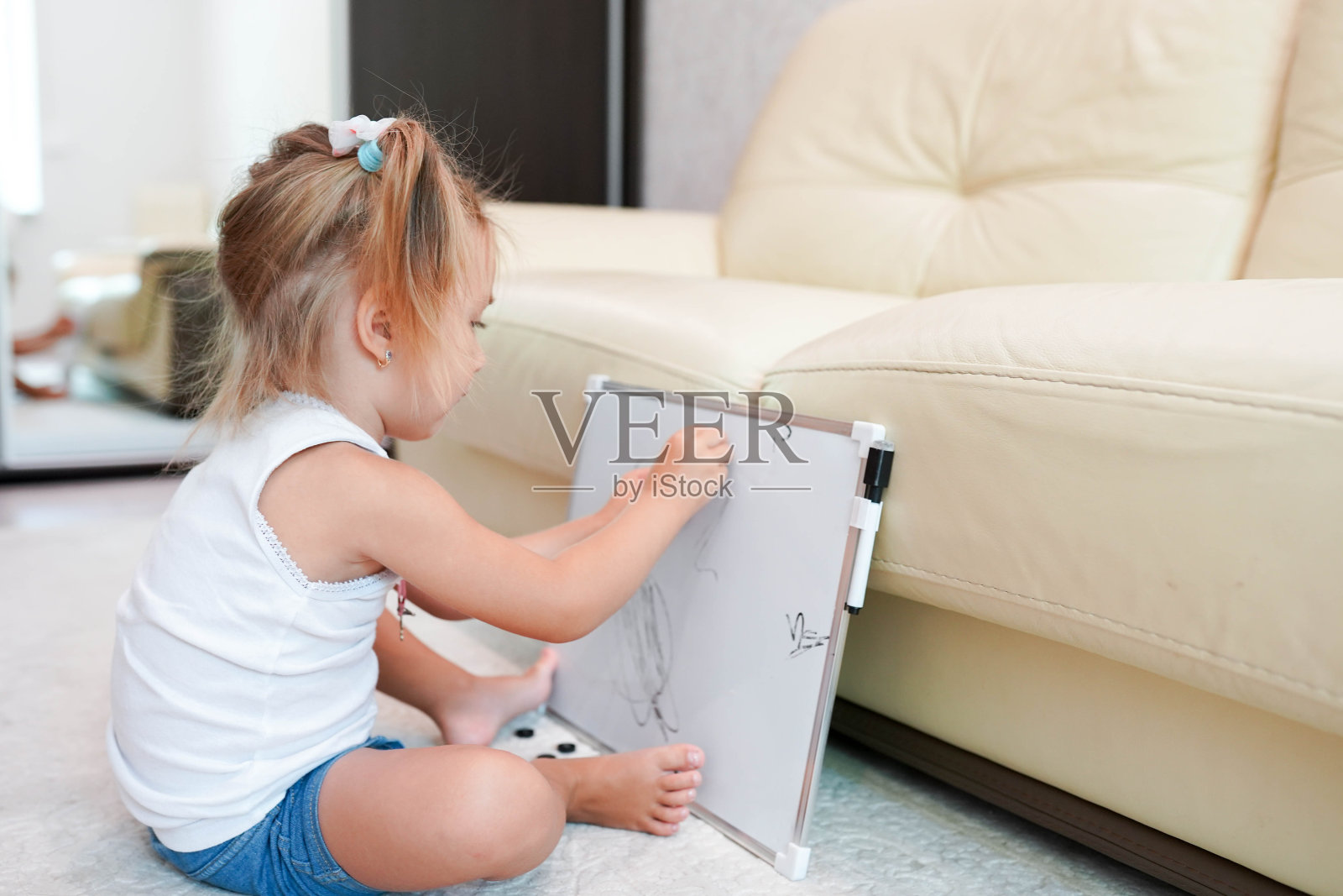 一个金发小女孩坐在家里的地板上在黑板上画画。照片摄影图片
