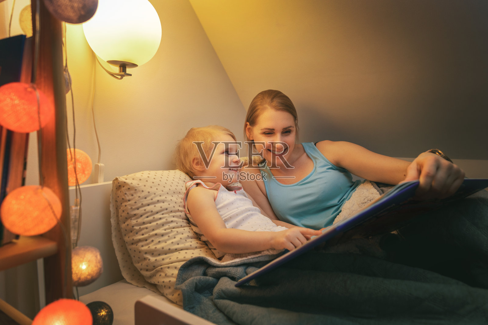 晚上睡觉前，妈妈和女儿一起在家里看童话尾巴书照片摄影图片