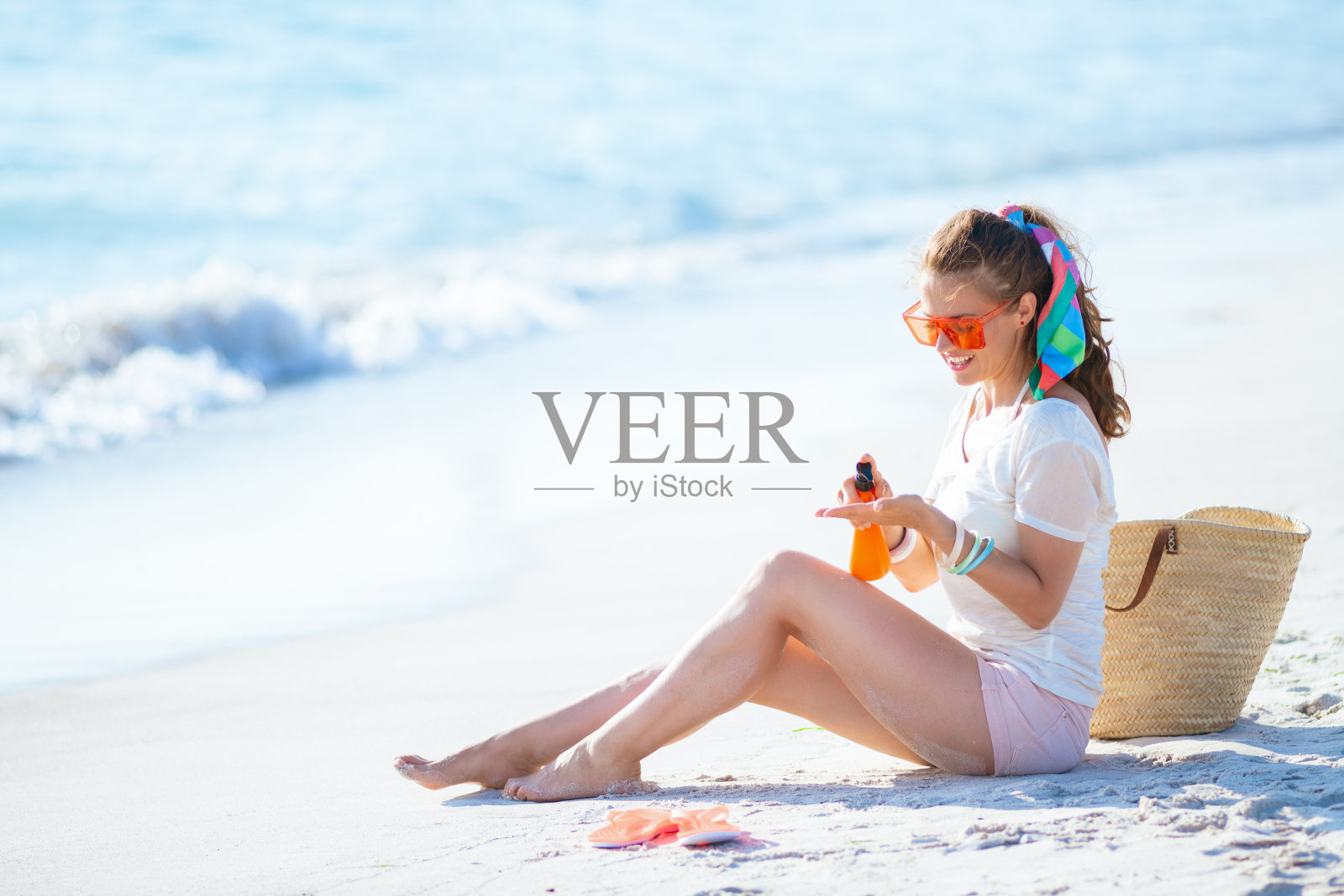 微笑的女人在涂抹防晒霜，而坐在海边照片摄影图片