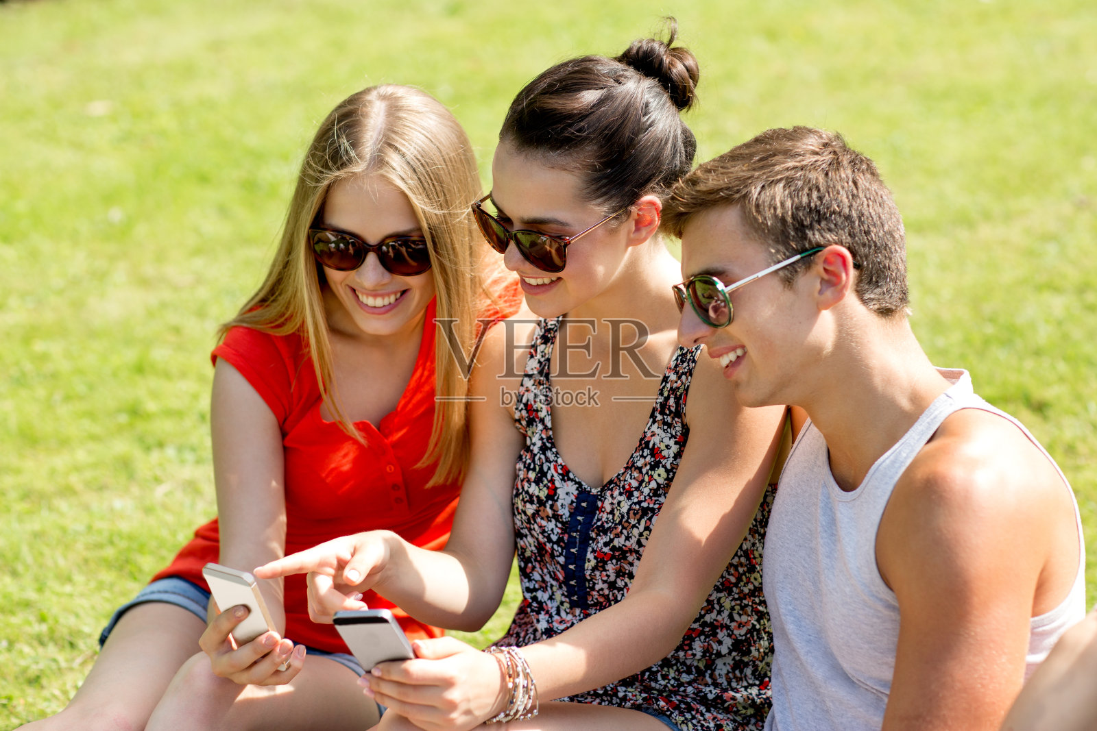 朋友们拿着智能手机坐在公园里微笑照片摄影图片