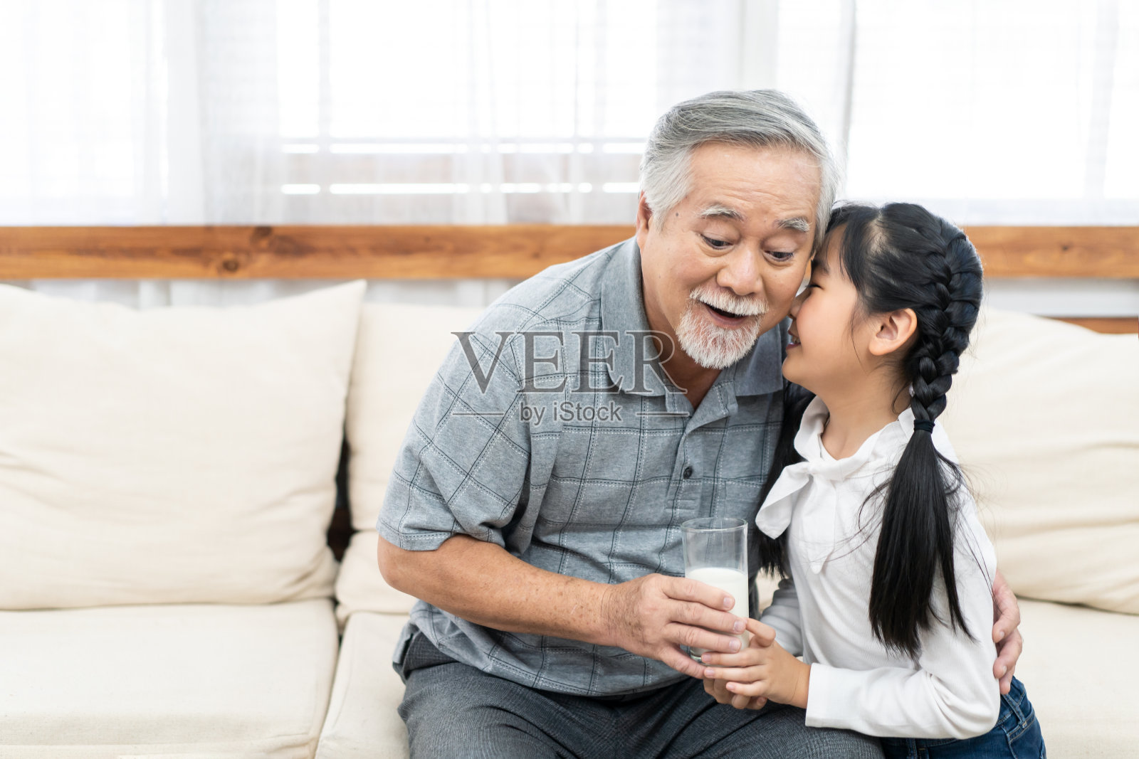 亚洲的小孙女给爷爷端来一杯牛奶。年轻的侄女女孩照顾爷爷亲吻他的幸福和微笑。老年医疗保健和老年家庭退休生活方式。照片摄影图片