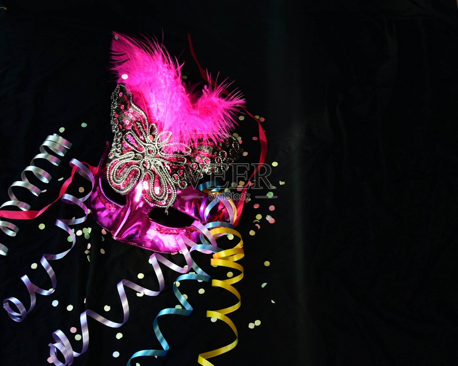 一个威尼斯狂欢节的粉色面具，黑色背景上点缀着羽毛、糊状物和糖果。有选择性的重点。巴西狂欢节是以面具和舞蹈为主题的庆祝活动。照片摄影图片