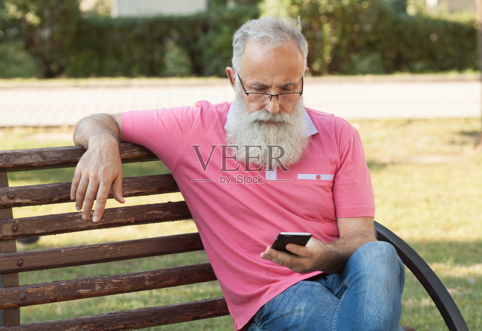 大胡子老人坐在长椅上用手机照片摄影图片