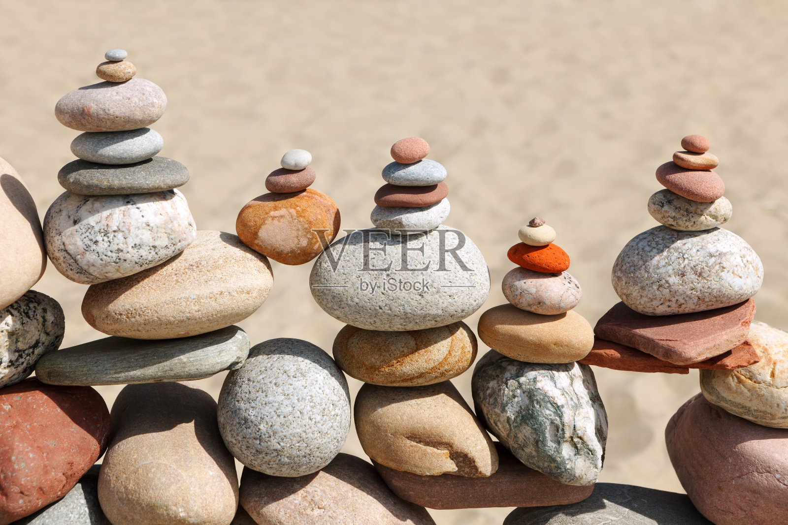 以沙滩为背景的沙滩上有许多平衡的、彩色的鹅卵石。照片摄影图片