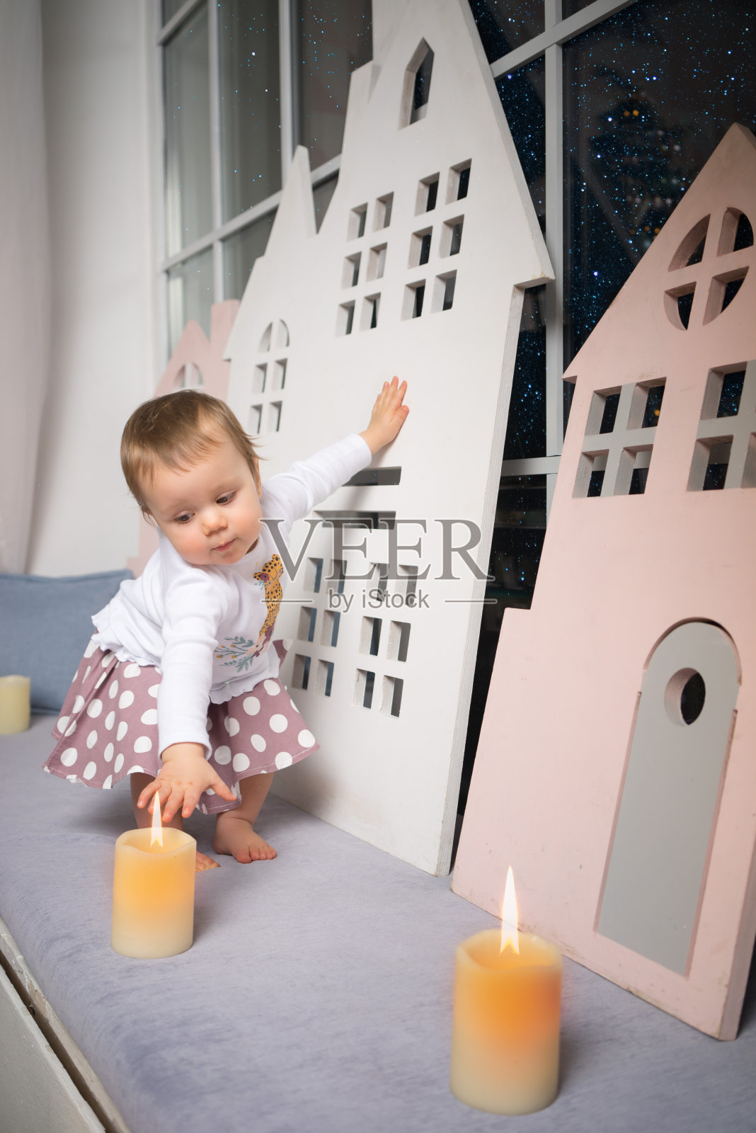 小女孩用蜡烛在室内靠近窗户的地方，用木头做玩具的房子。抵押贷款的概念。照片摄影图片