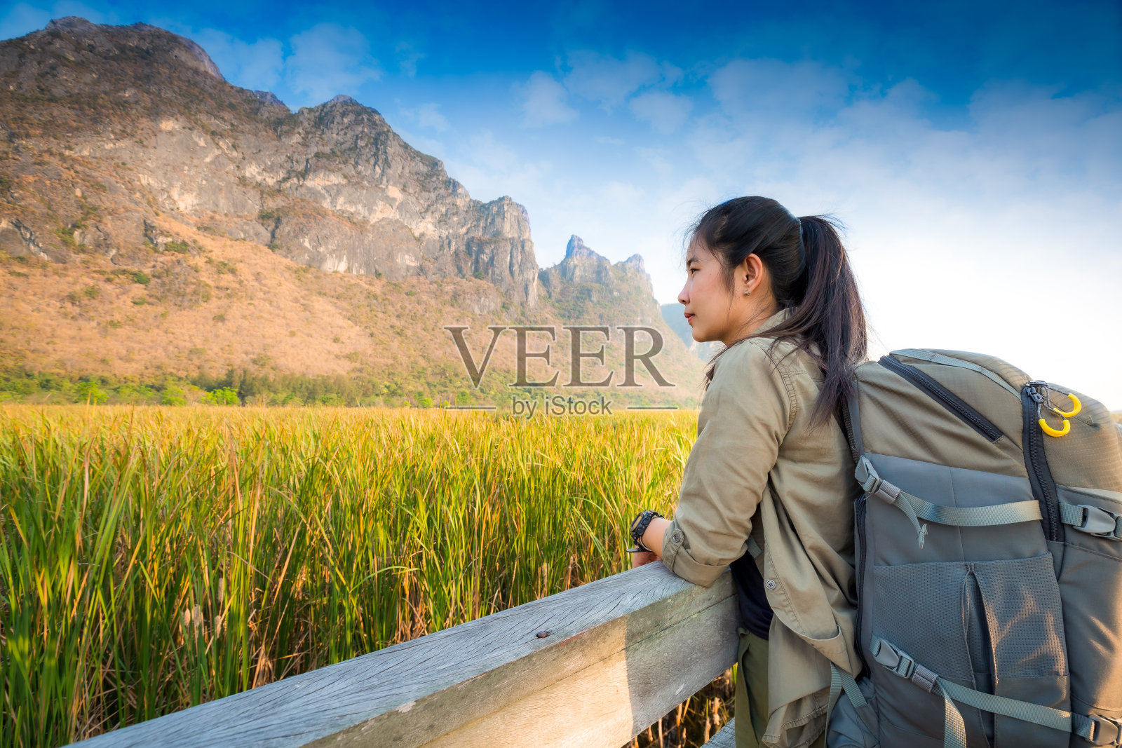 亚洲徒步旅行者背着沉重的背包，在一个小亭子户外徒步小径上的木桥上，沼泽与草地和蓝山背景。Khao Sam Roi Yot国家公园。照片摄影图片