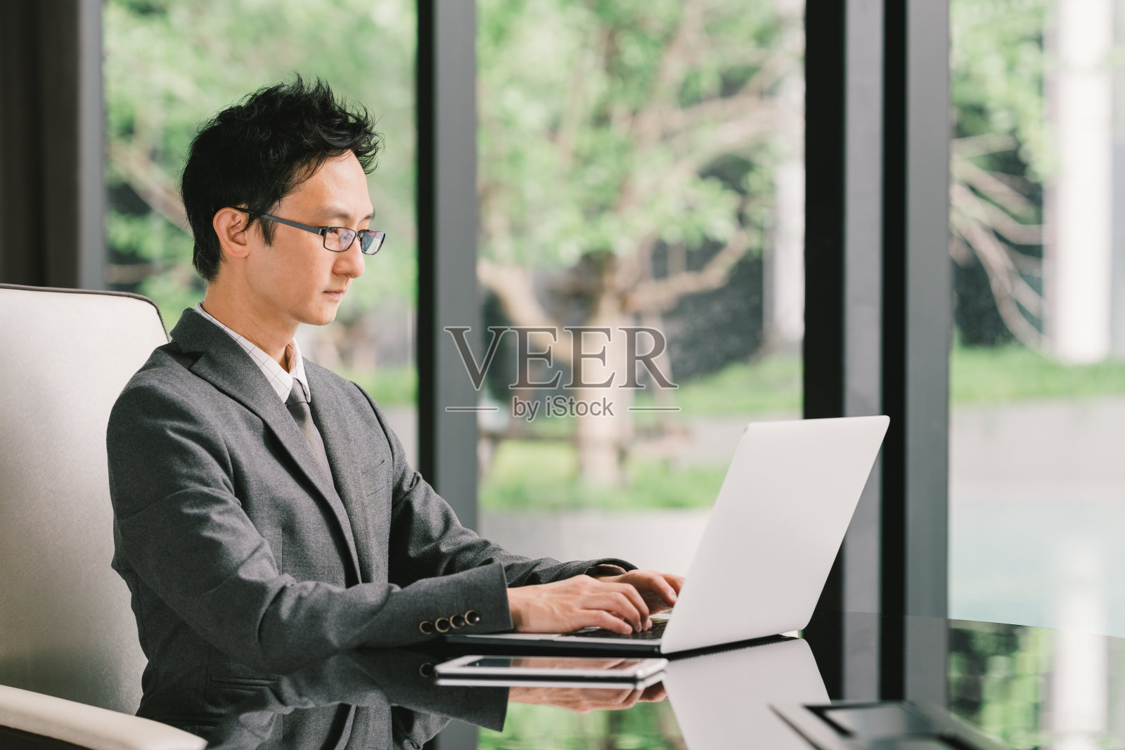 英俊的亚洲商人或企业家，在行政办公室使用笔记本电脑和数字平板电脑。领导力，商业沟通，创业，或信息技术小工具的概念照片摄影图片