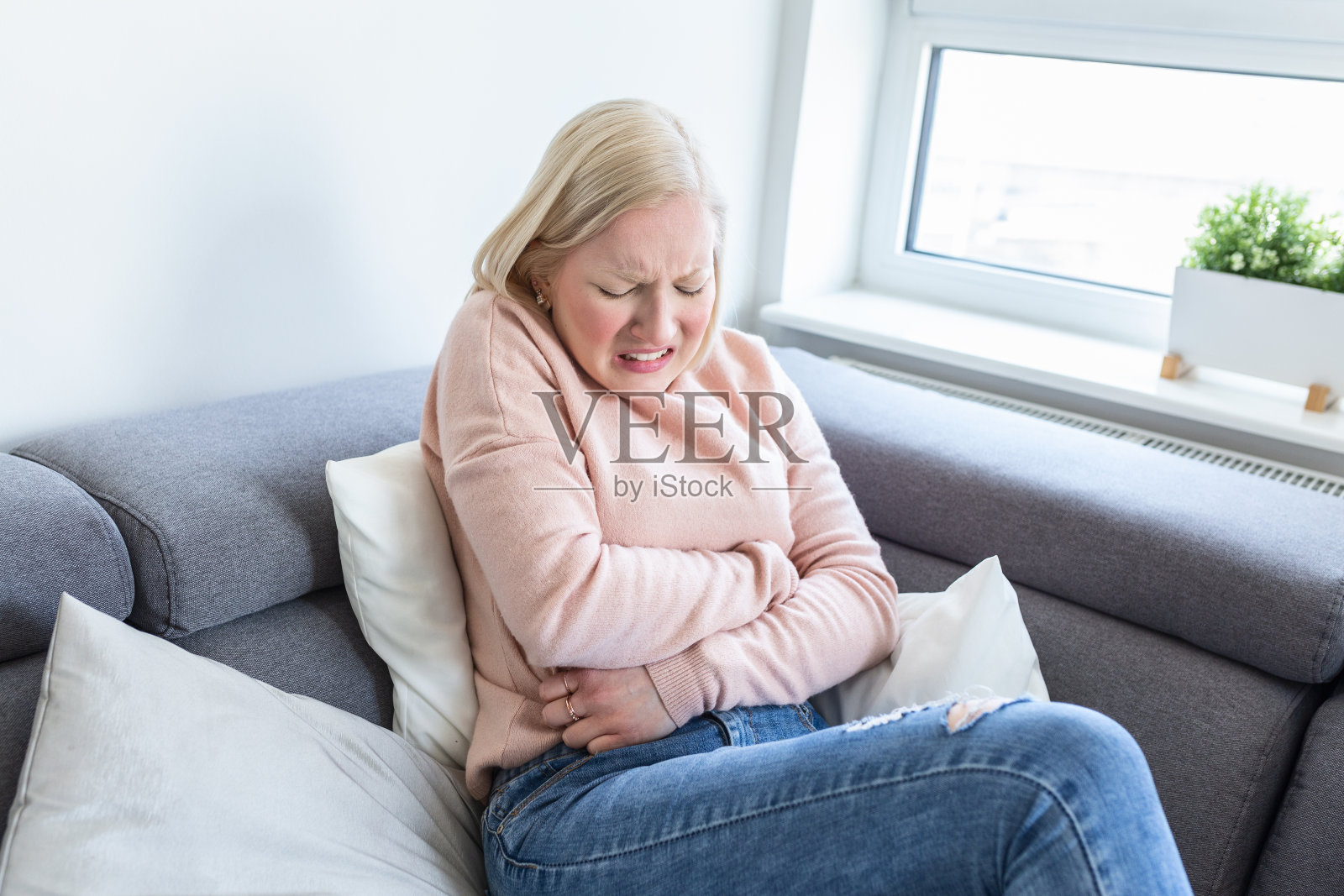 观的年轻女子在家里的沙发上遭受胃痛。女人坐在床上，肚子疼。一名年轻女子坐在家里的沙发上忍受着腹痛照片摄影图片
