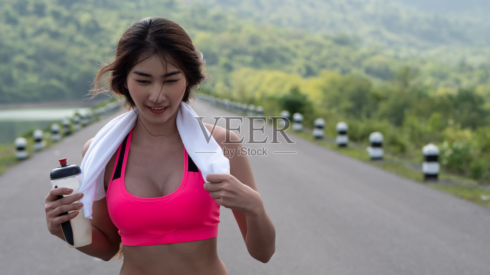 近景:年轻的亚洲妇女在户外晨光中奔跑。女性慢跑者在户外拿着瓶装水锻炼。健康生活方式照片摄影图片