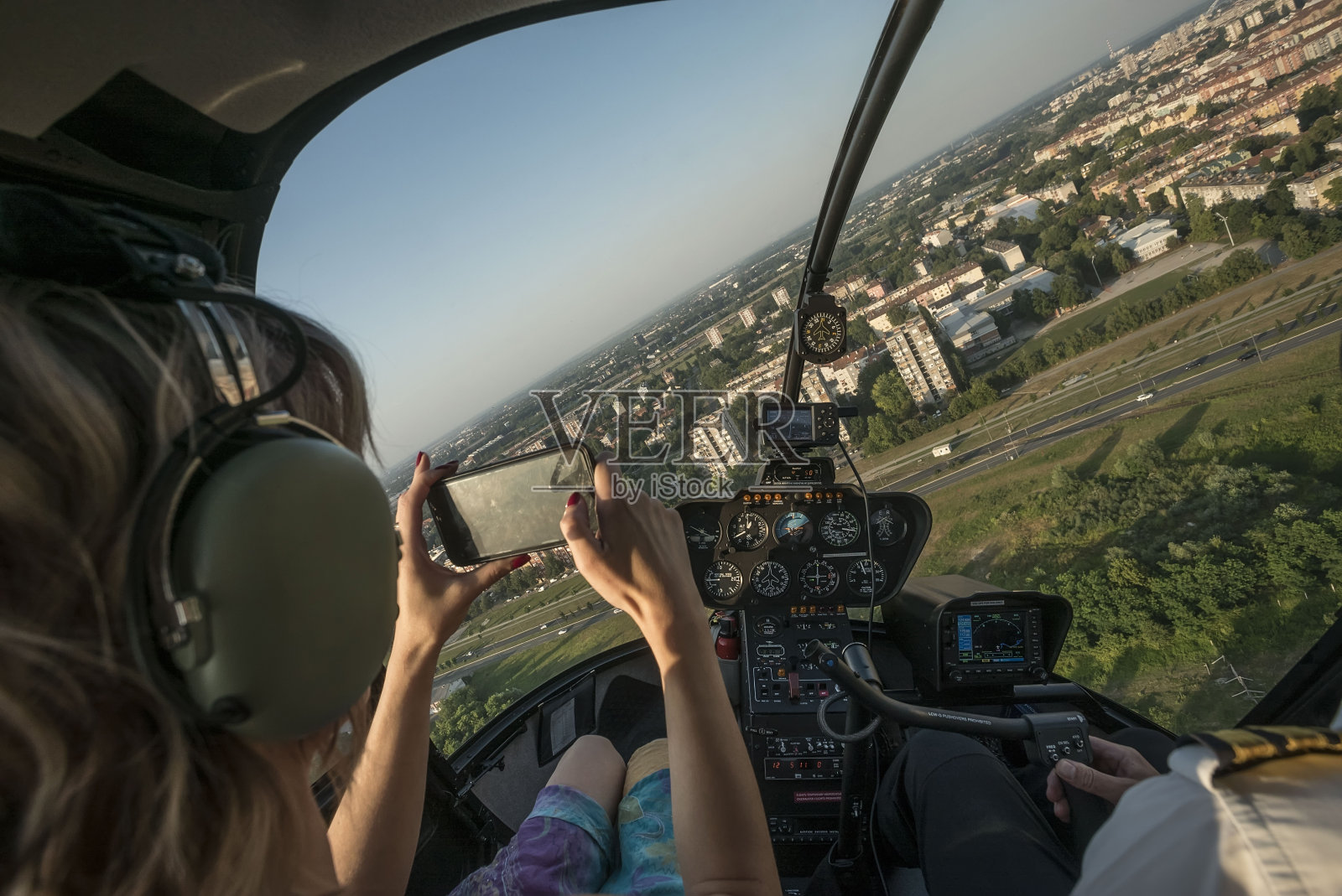 美丽的金发女人在直升机上用智能手机拍摄城市风景。照片摄影图片