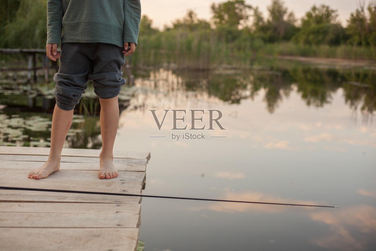 孩子的腿在湖的背景上。孩子站在木码头上。照片摄影图片