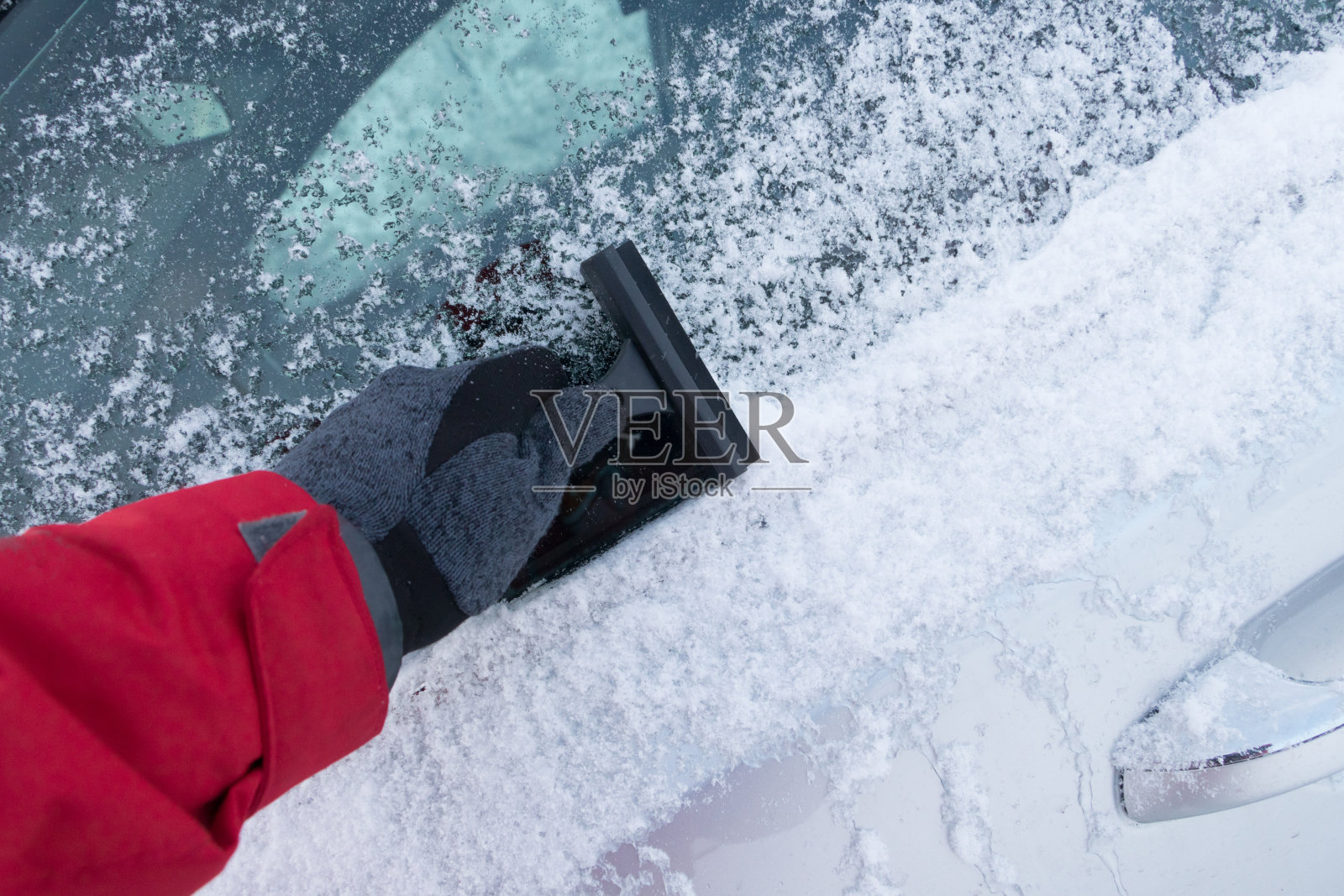 冬天的暴风雪使汽车被雪覆盖。男人的手在开车前清理汽车挡风玻璃上的雪。降雪气候问题照片摄影图片