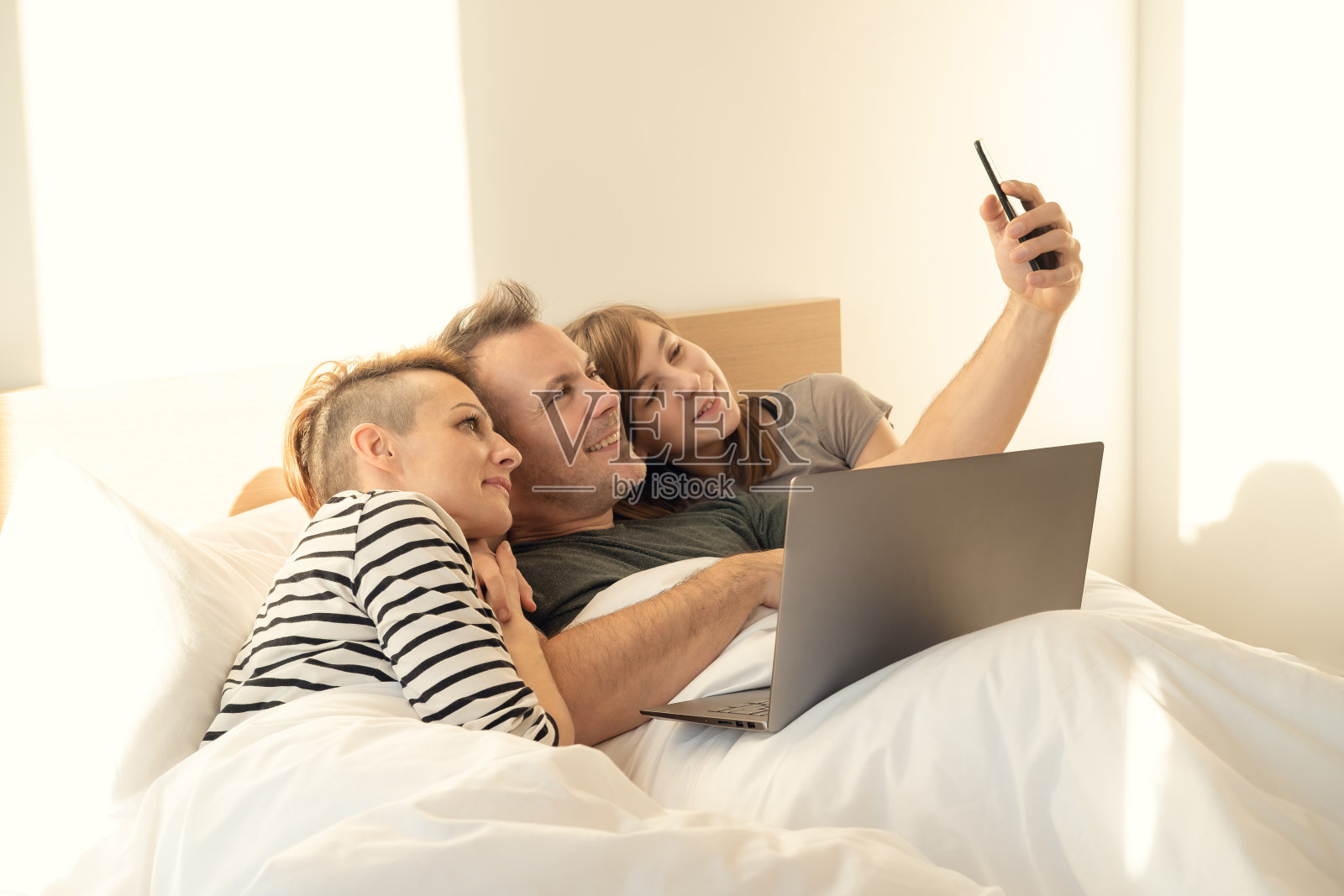 快乐的家人用手机自拍。家人躺在床上自拍。照片摄影图片