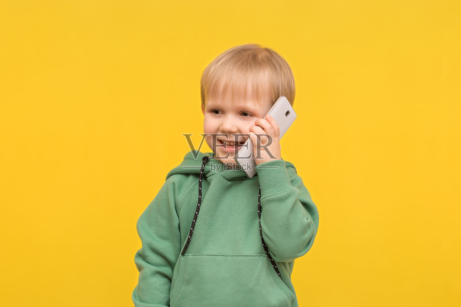 金发的小男孩正在用黄色的春天背景下的智能手机打电话。照片摄影图片