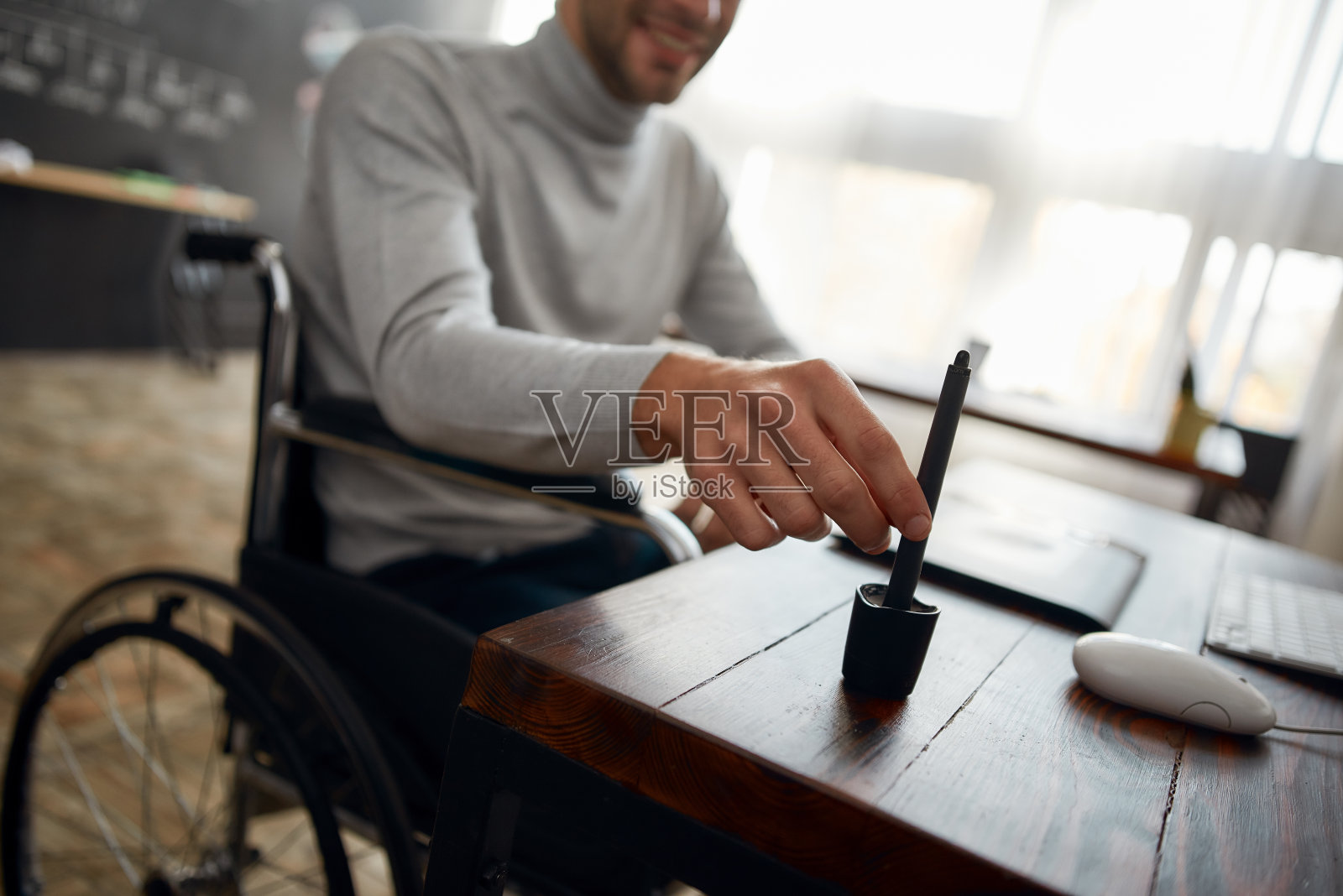 裁剪照片的年轻设计师在轮椅上使用手写笔和数字平板电脑，而在现代办公室工作。设计工作室照片摄影图片
