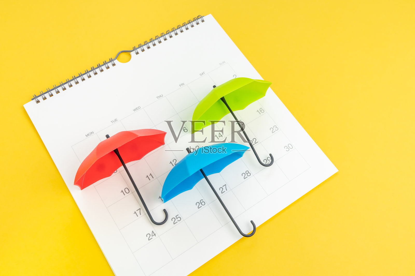 假日季节，夏雨季节日历概念，彩色小伞上白色干净的日历上黄色的背景照片摄影图片