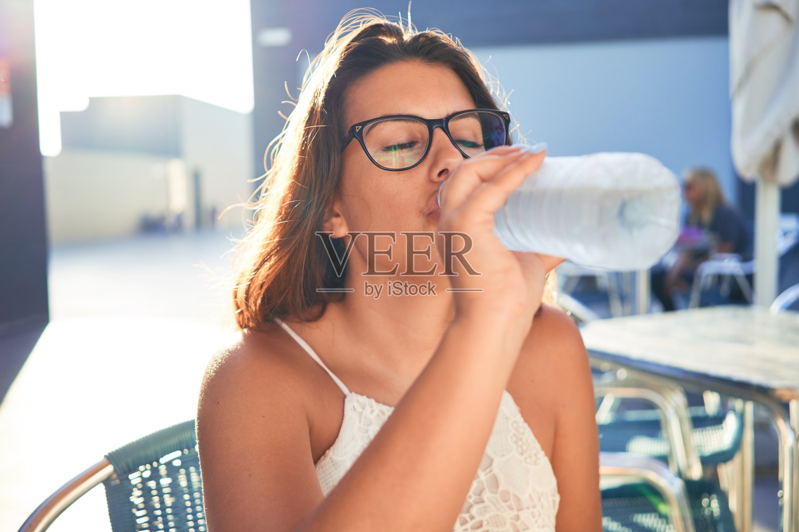 年轻漂亮的女人坐在餐厅里喝着一瓶水享受暑假照片摄影图片