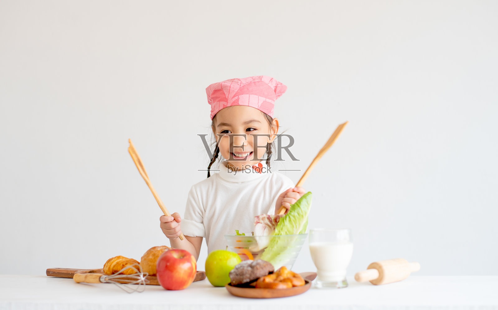亚洲小女孩厨师拿着勺子，看着她的右边和微笑与概念快乐的小厨师。照片摄影图片