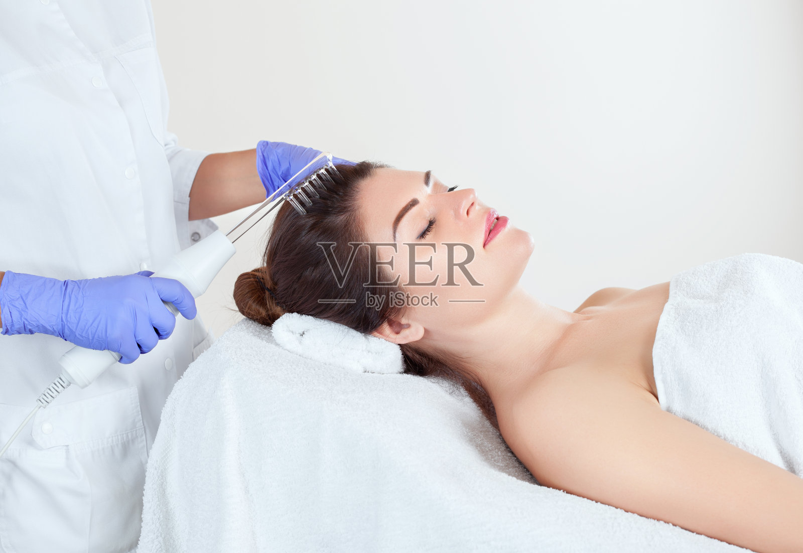 在美容院，医生兼美容师在一位年轻美丽的女士的头皮上做微电流治疗。美容和专业皮肤护理。照片摄影图片