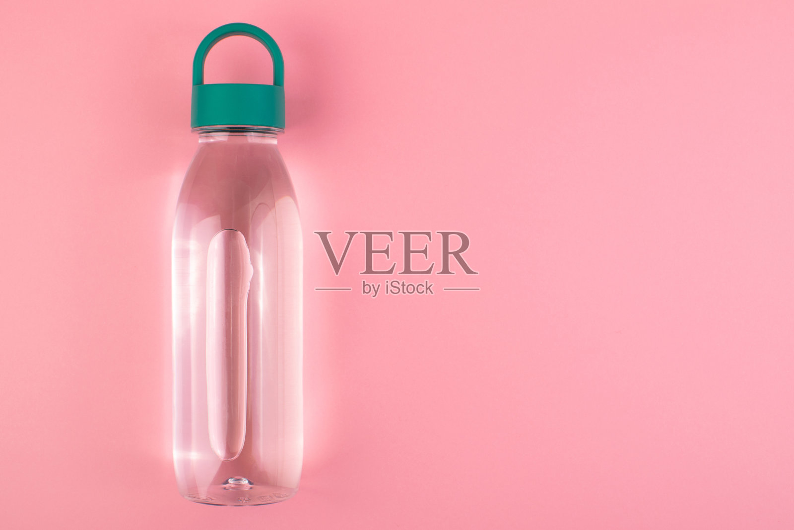 一个可重复使用的塑料水瓶，绿色的盖子，粉红色的背景。简约的健康的生活方式。照片摄影图片
